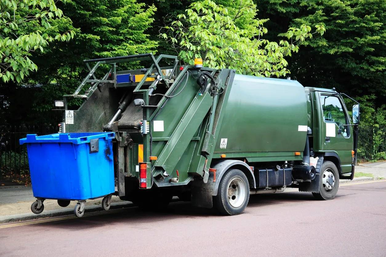 A garbage truck is parked next to a dumpster.